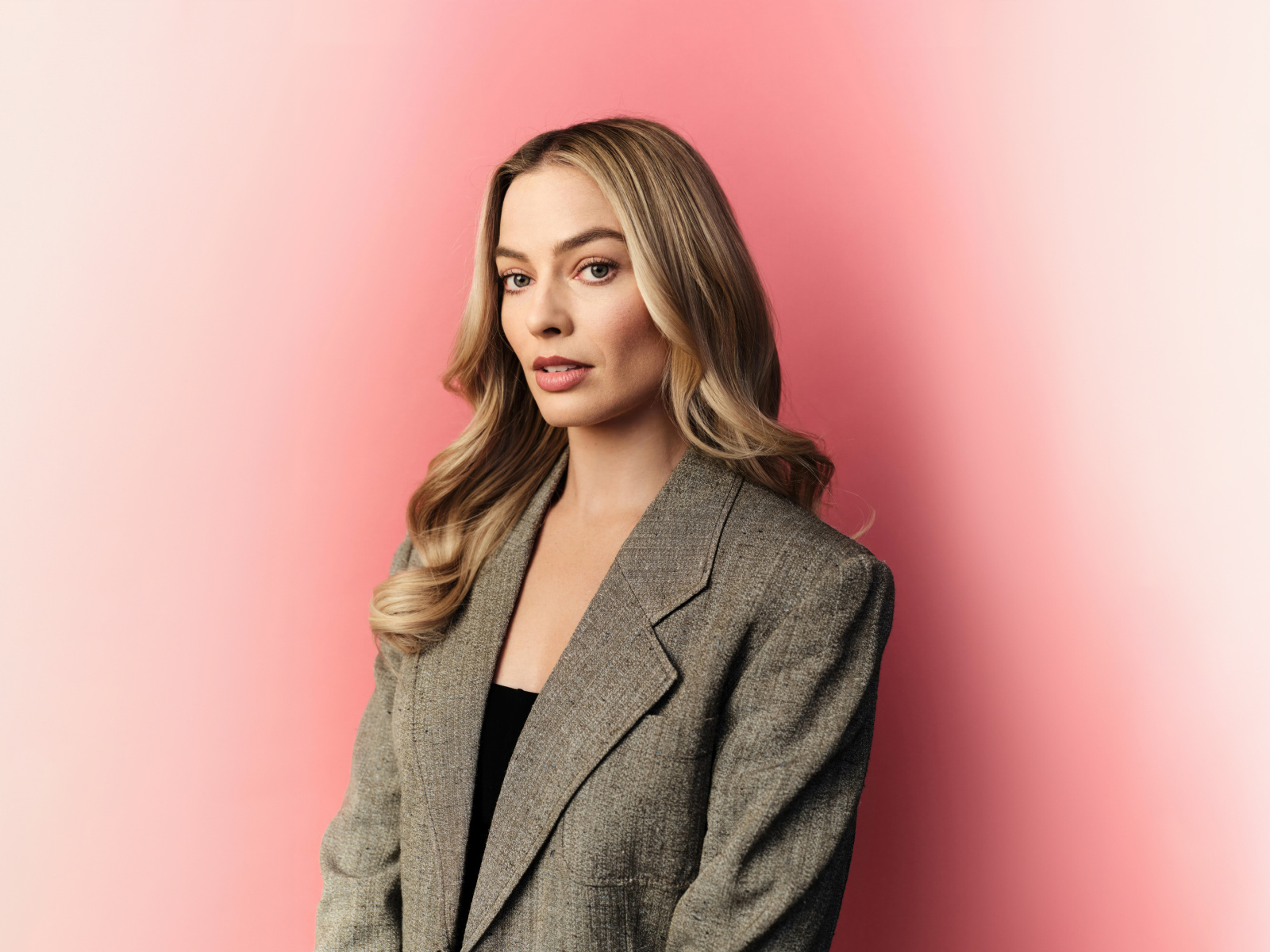 Актриса Марго Робби в сером пиджаке на розовом фоне