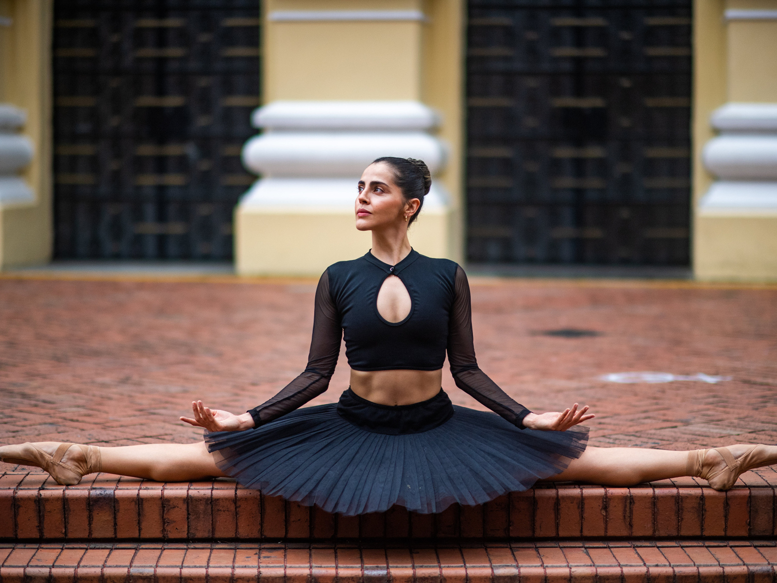 Девушка балерина в черном сидит на шпагате
