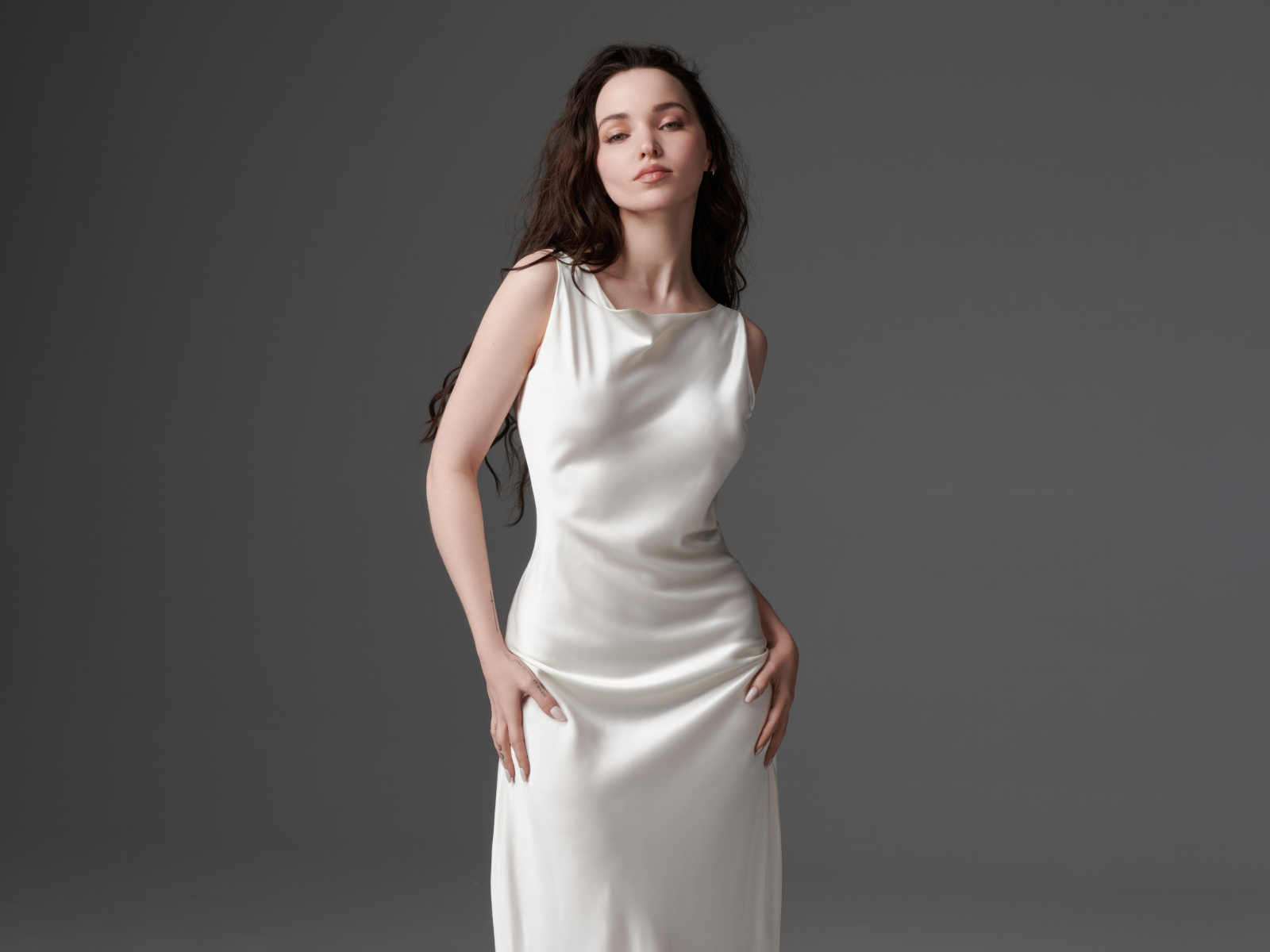 Стройная девушка актриса Дав Кэмерон в белом платье на сером фоне