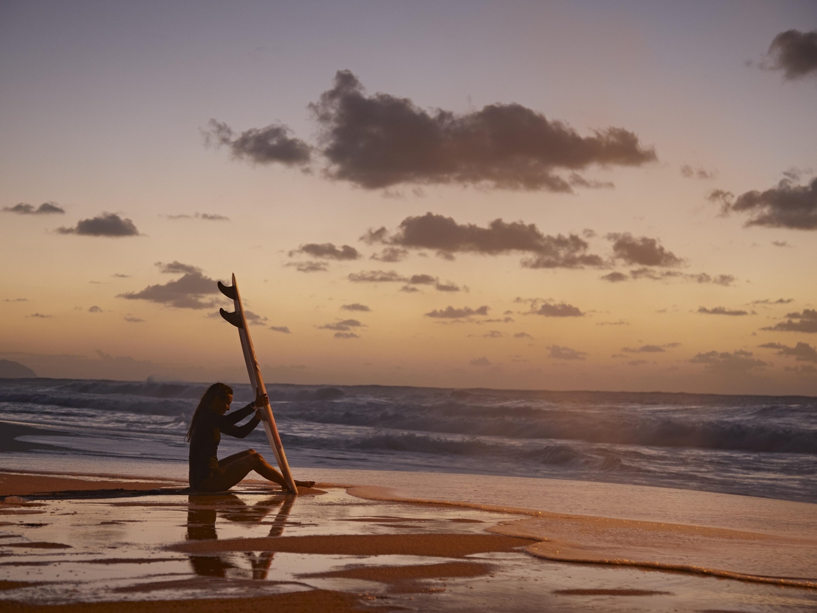 Девушка серфингистка сидит на берегу моря