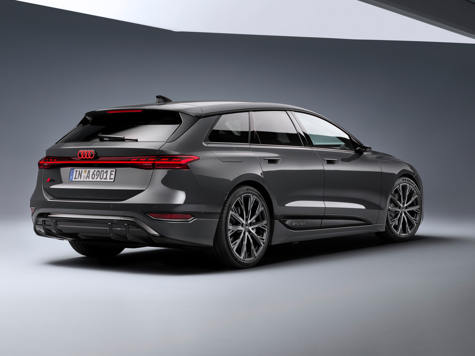 Автомобиль Audi A6 Avant e-tron S line 2024 года на сером фоне вид сзади