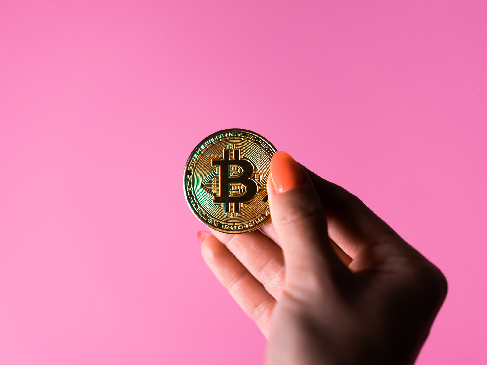 Золотая монета биткоин в руке девушки на розовом  фоне
