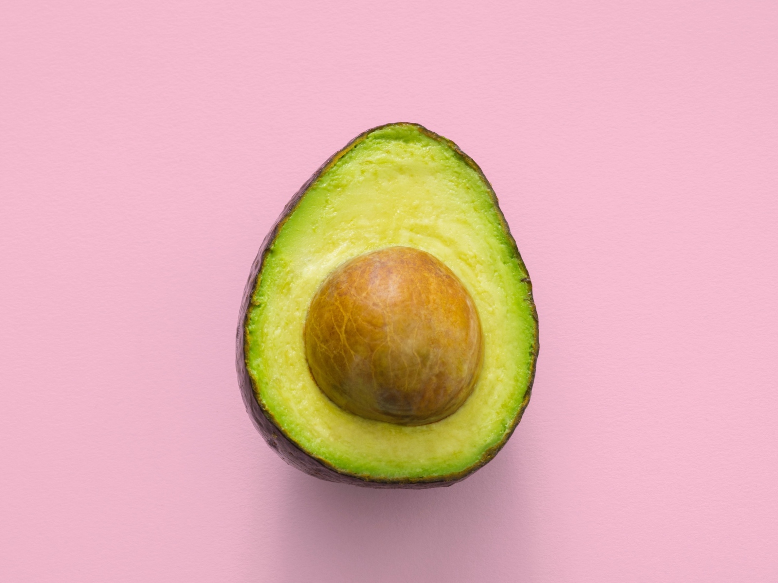 Половина авокадо с большой косточкой на розовом фоне