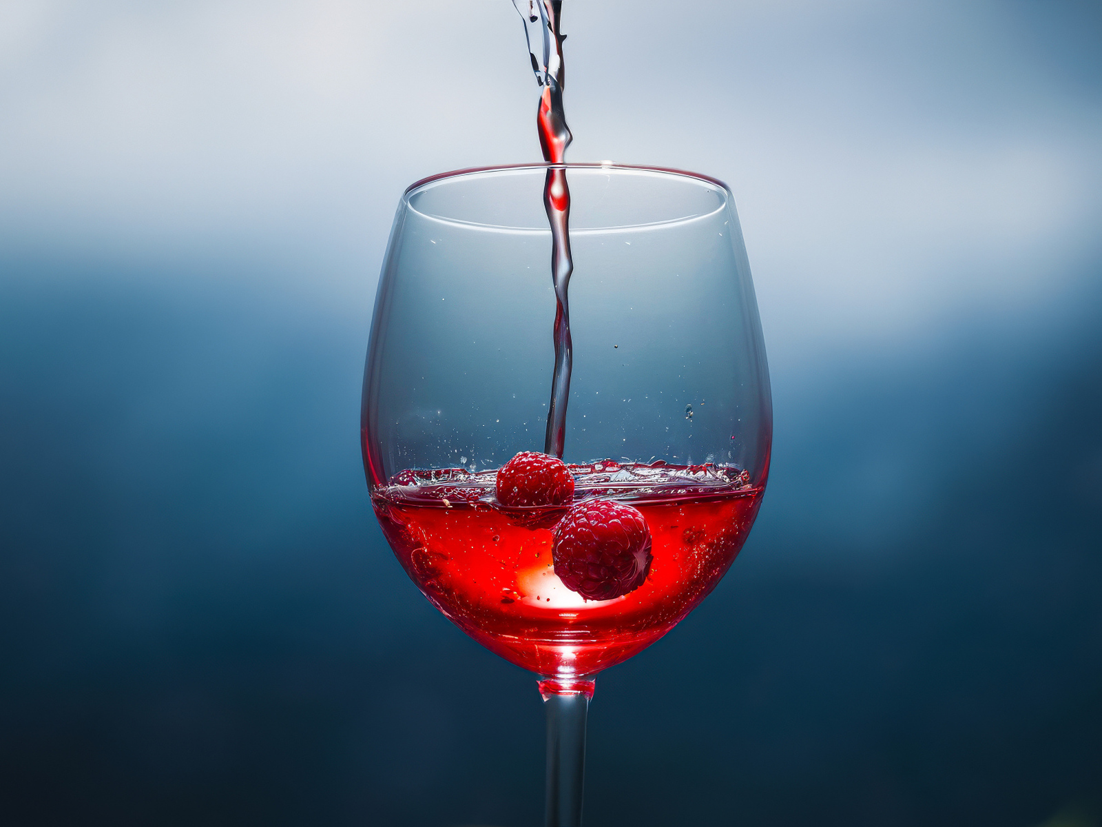 Вино наливают в бокал с ягодами малины на сером фоне