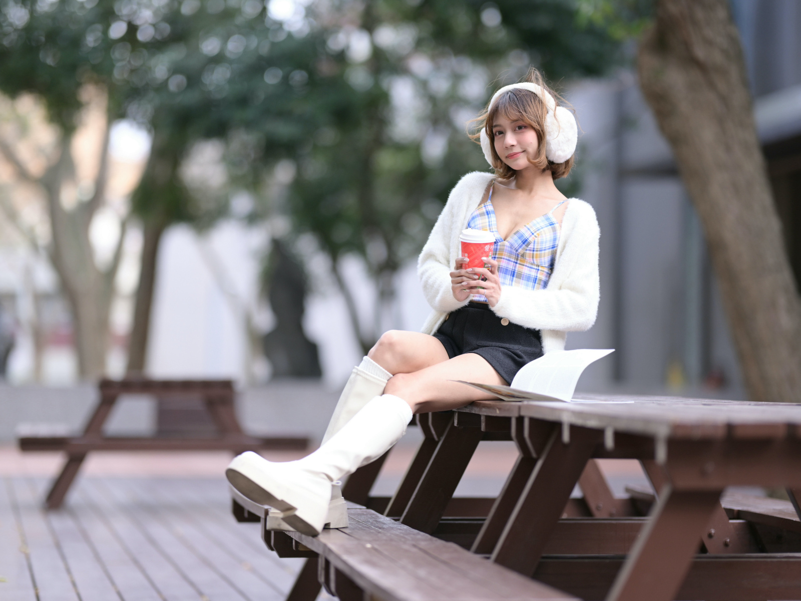 Девушка азиатка с кофе сидит на столе в парке