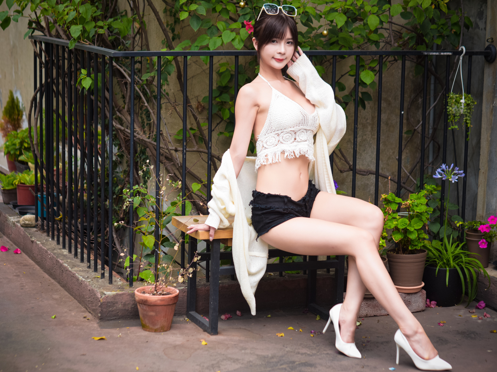 Стройная девушка азиатка сидит на лавке у дома