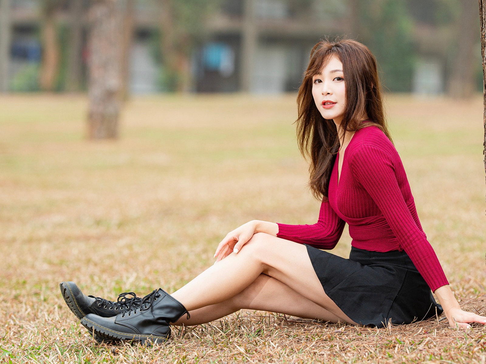 Молодая азиатка в красном свитере сидит под деревом