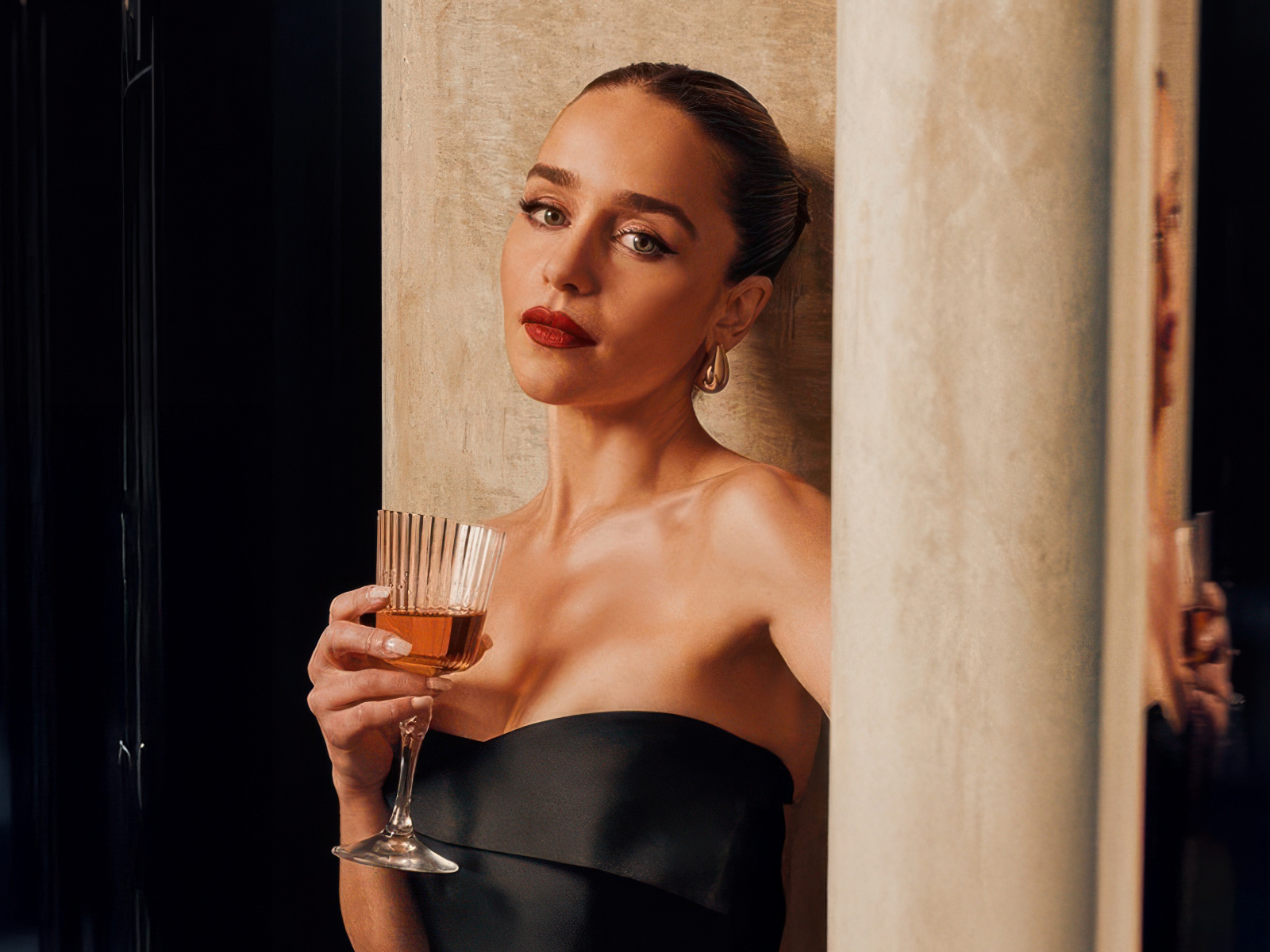 Актриса Эмилия Кларк с бокалом стоит у стены