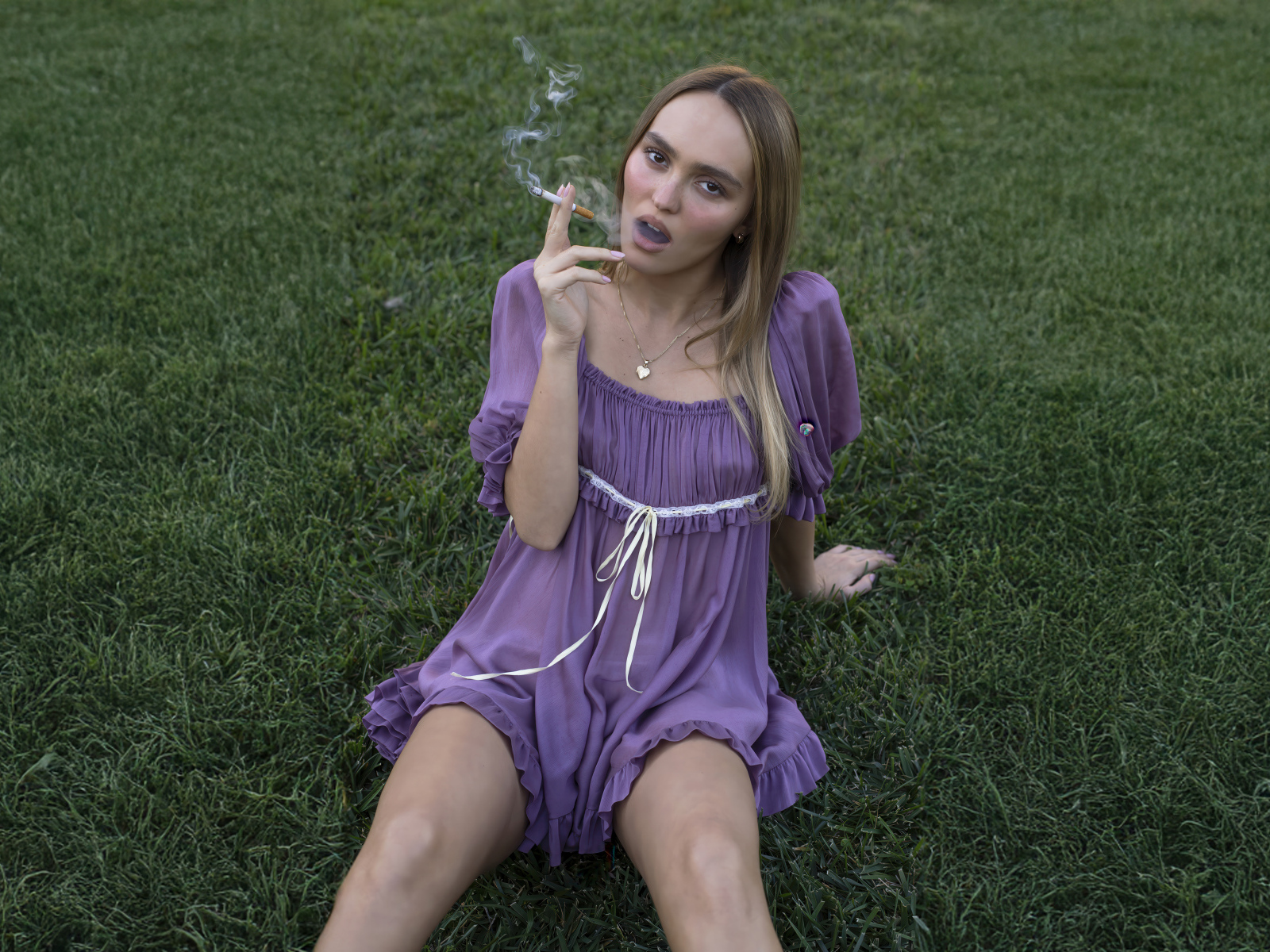 Молодая Лили-Роуз Депп с сигаретой сидит на траве