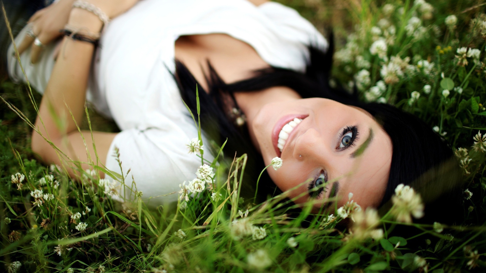 Девушка брюнетка с пирсингом в носу лежит в траве