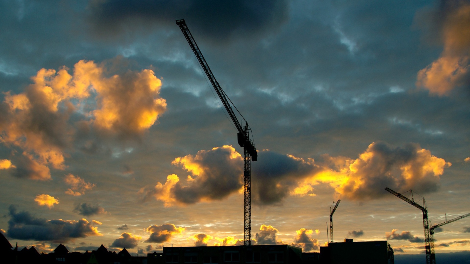 Стрелы кранов на стройке на фоне облаков