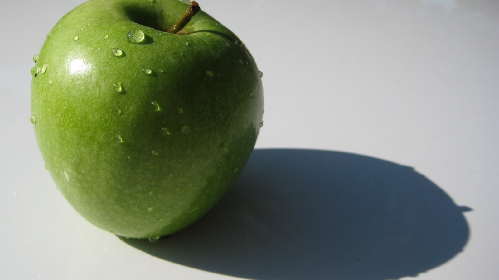 Зеленое яблоко на белой поверхности