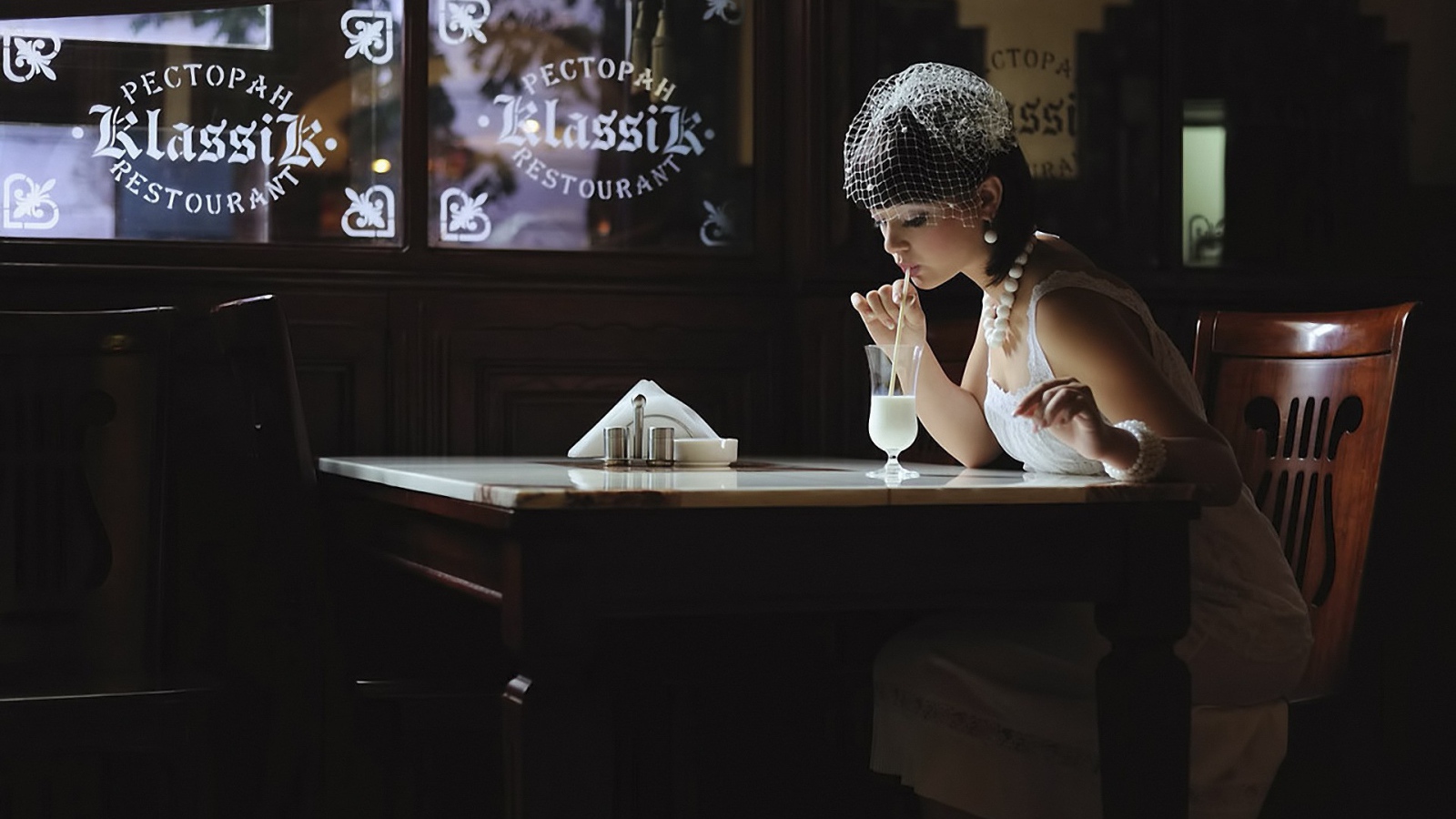 Девушка в белом платье пьет коктейль в ресторане