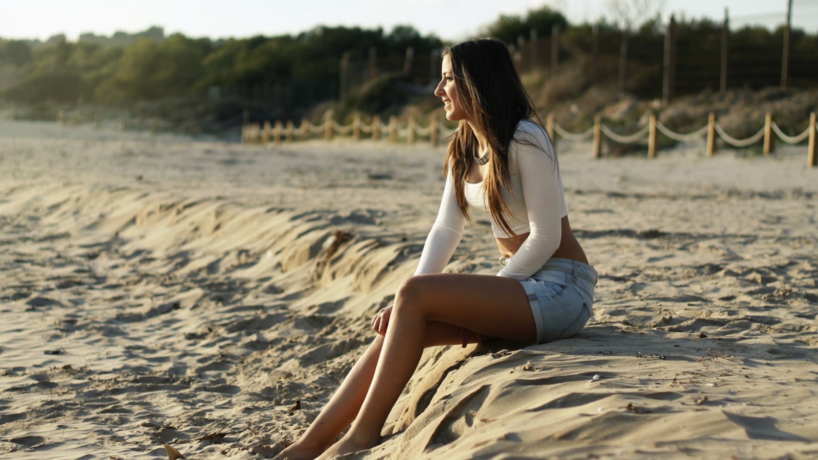 Девушка в джинсовых шортах сидит на песке пляжа