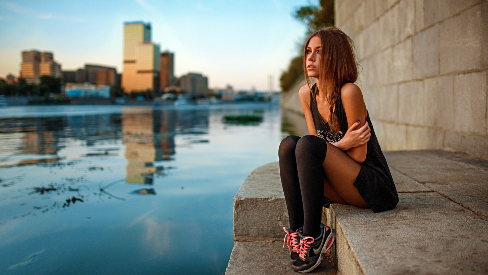 Девушка в кедах сидит на набережной