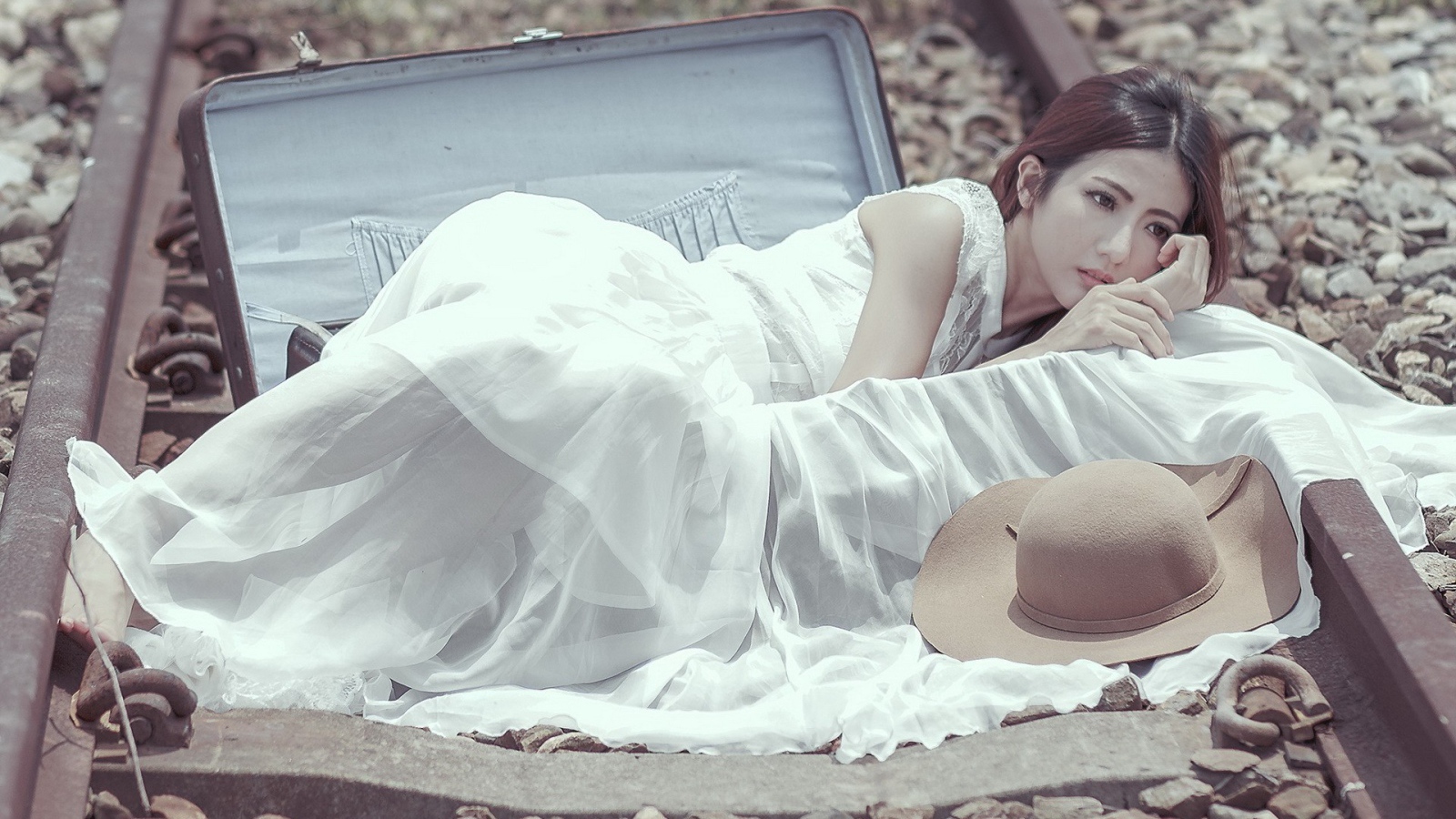 Девушка лежит в чемодане на рельсах