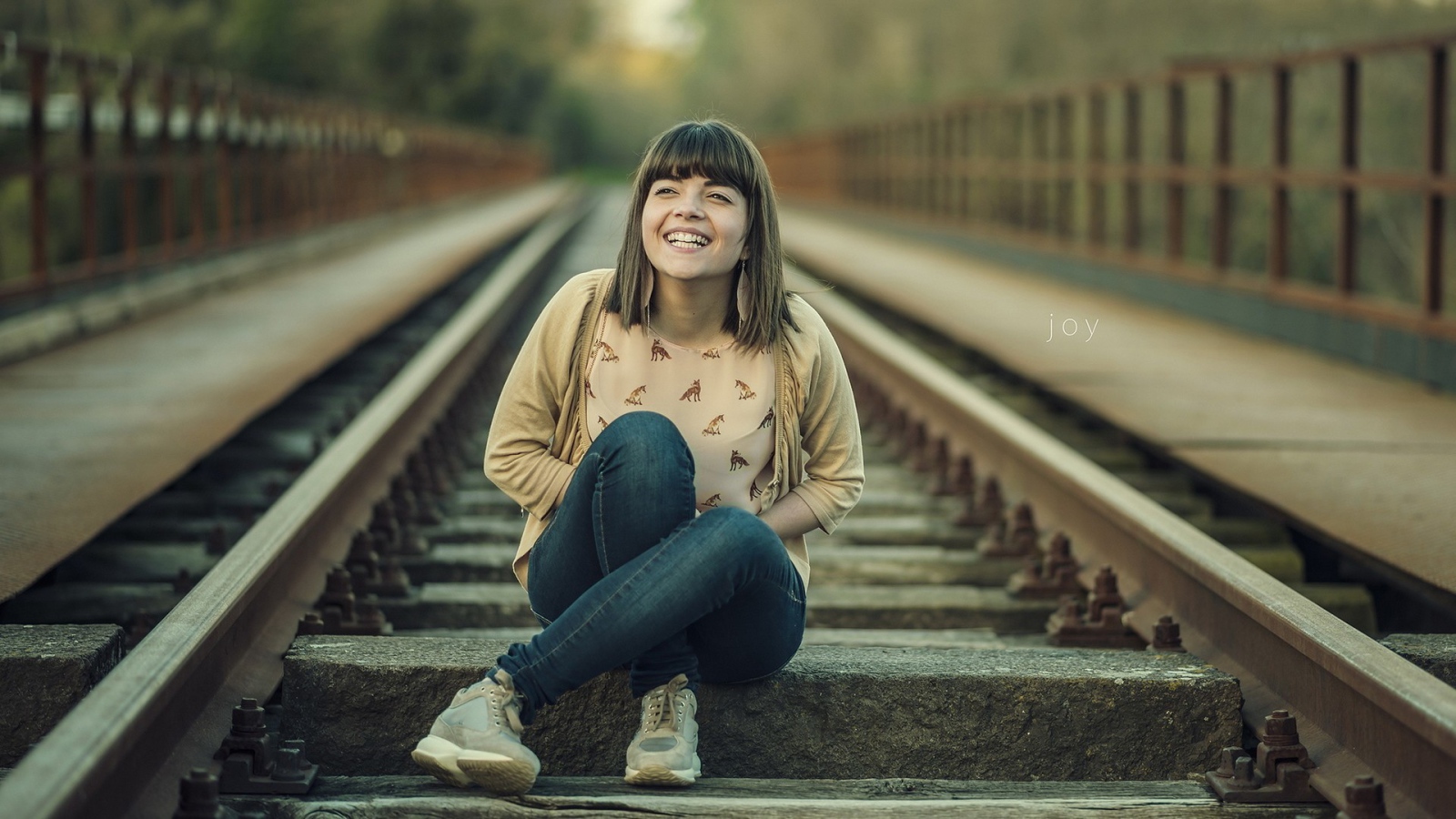 Девушка улыбается сидя на рельсах