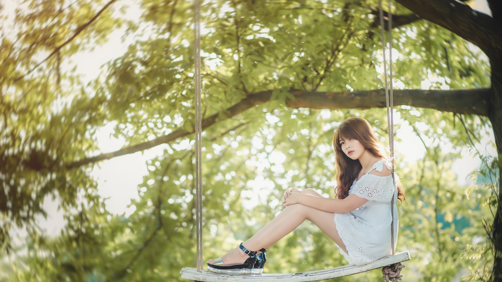 Японская девушка в белом платье сидит на качелях