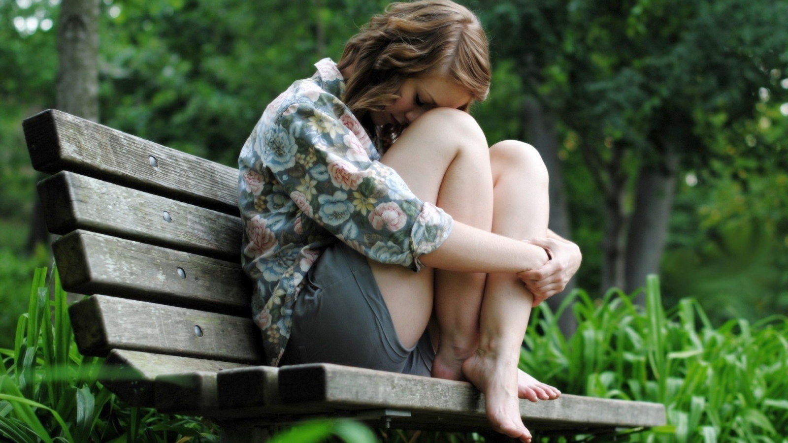 Девушка грустит сидя на скамье