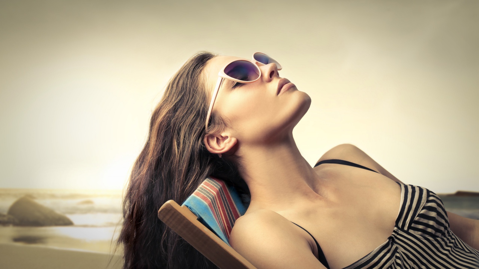 Девушка в очках загорает в шезлонге