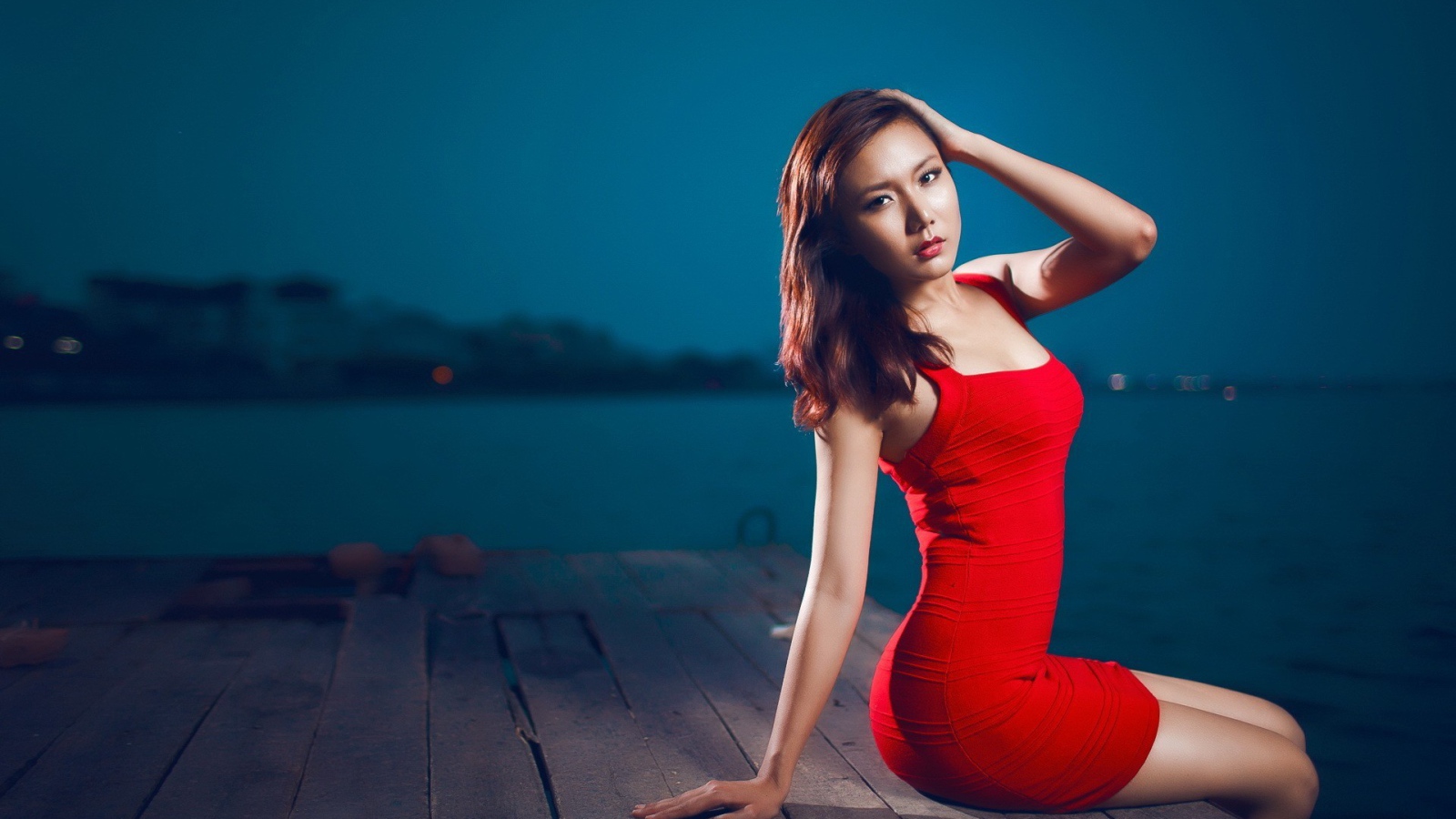 The girl in the red dress sitting on the edge of a wooden jetty