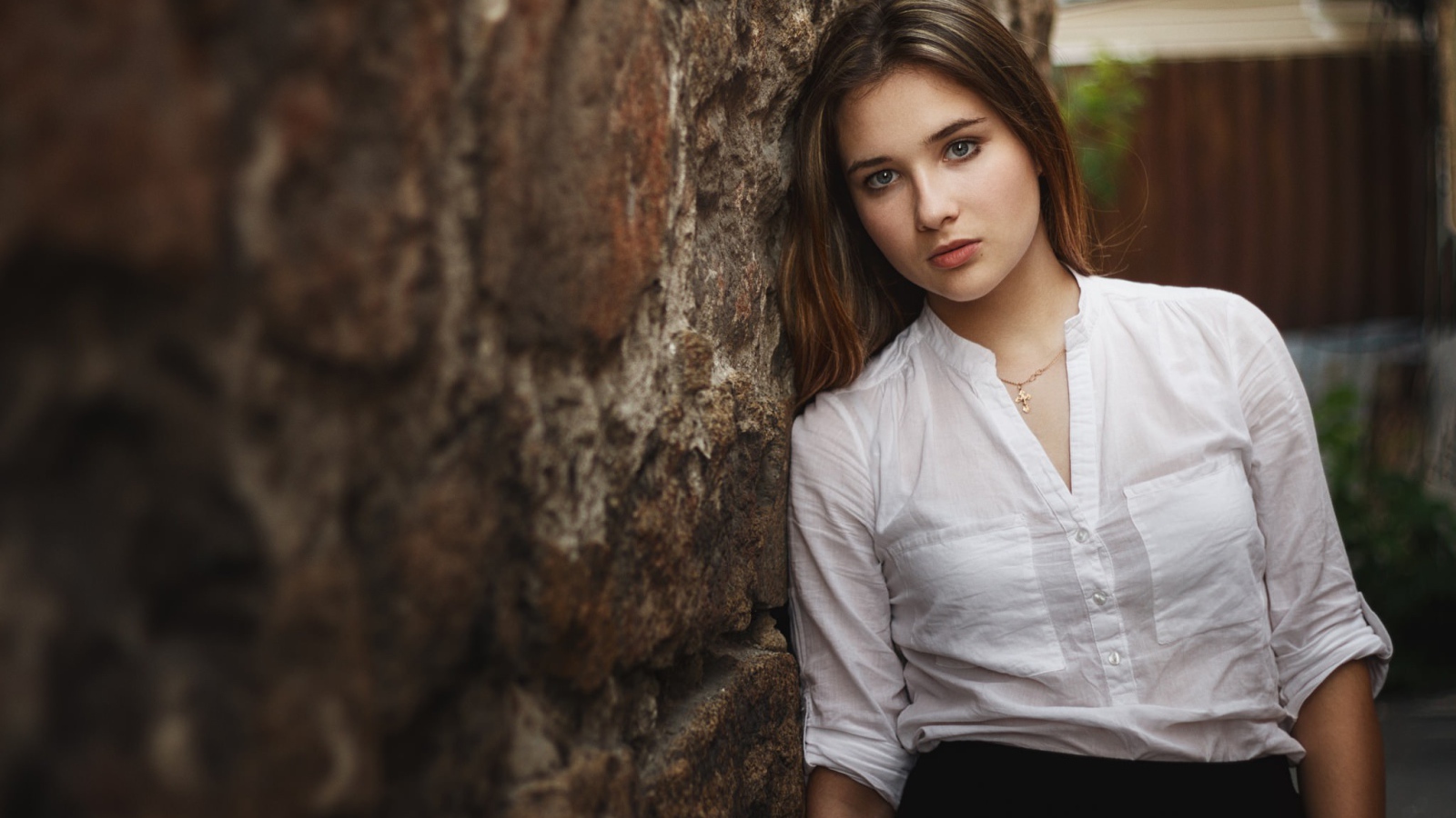Девушка в белой рубашке стоит у стены