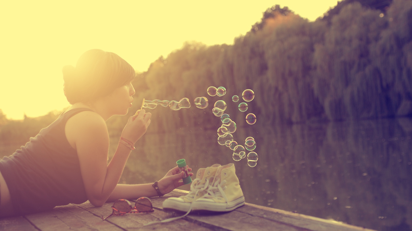 Девушка лежит на пирсе и играет с мыльными пузырями