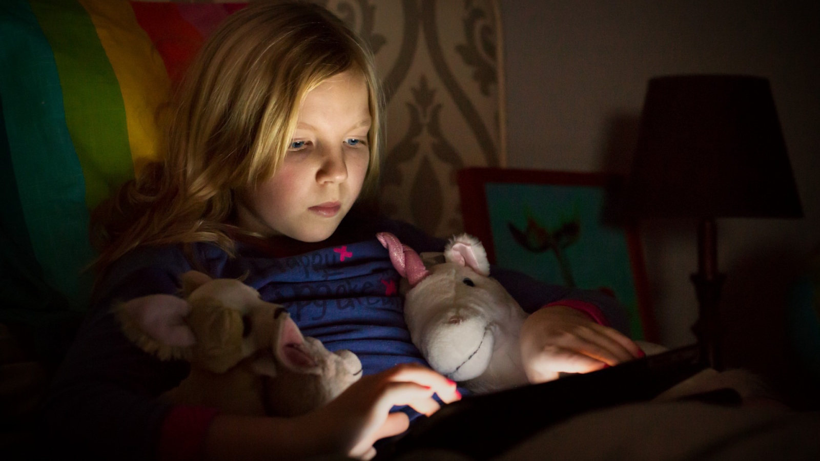 Девочка играет с планшетом лежа в кровати