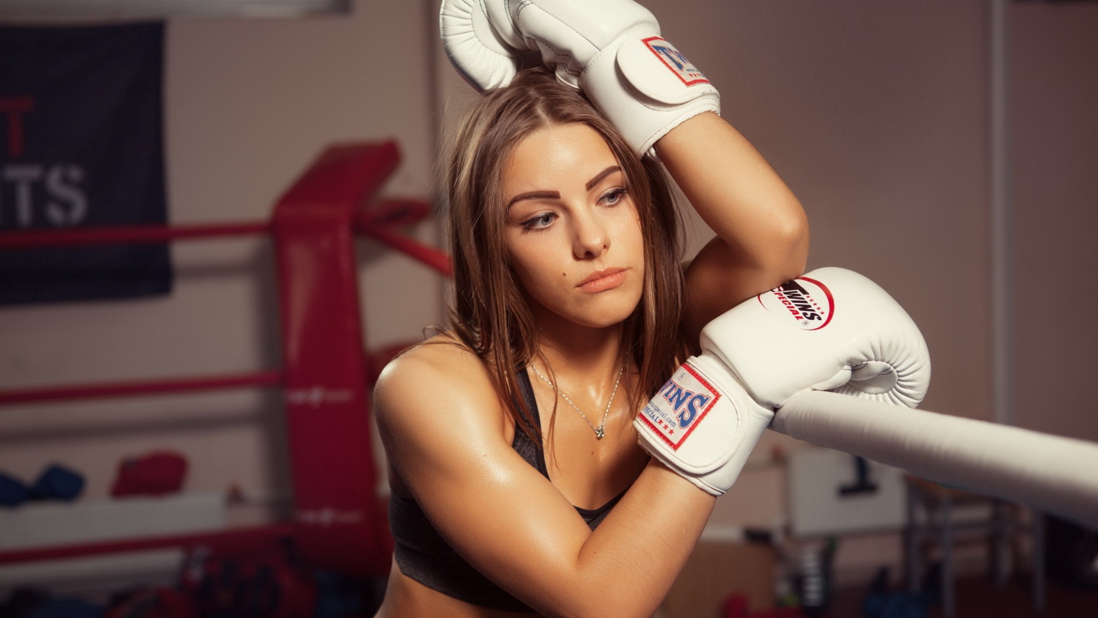 Девушка в белых перчатках отдыхает у канатов ринга