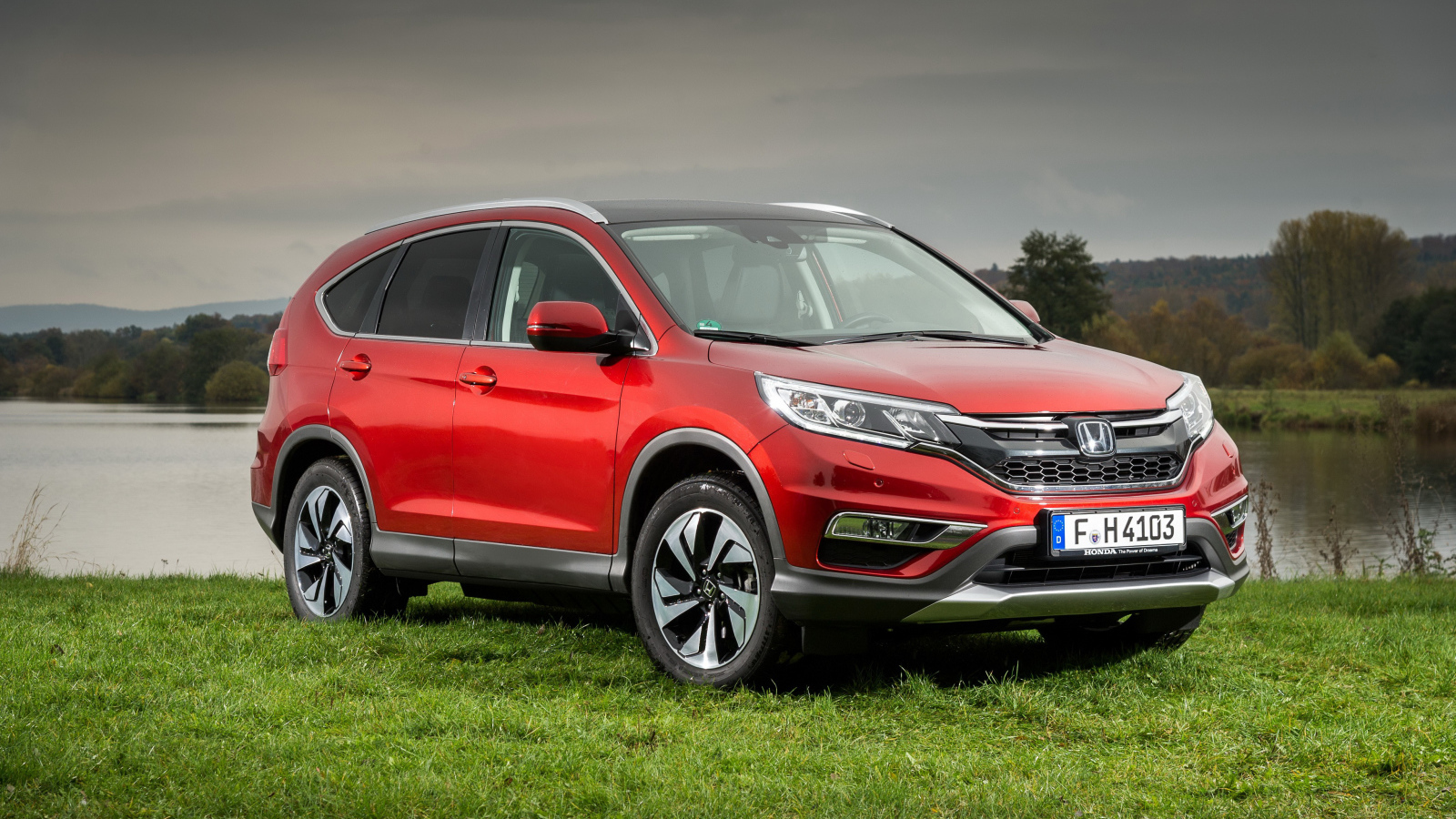 Красный внедорожник Honda CR-V стоит на зеленой траве у реки