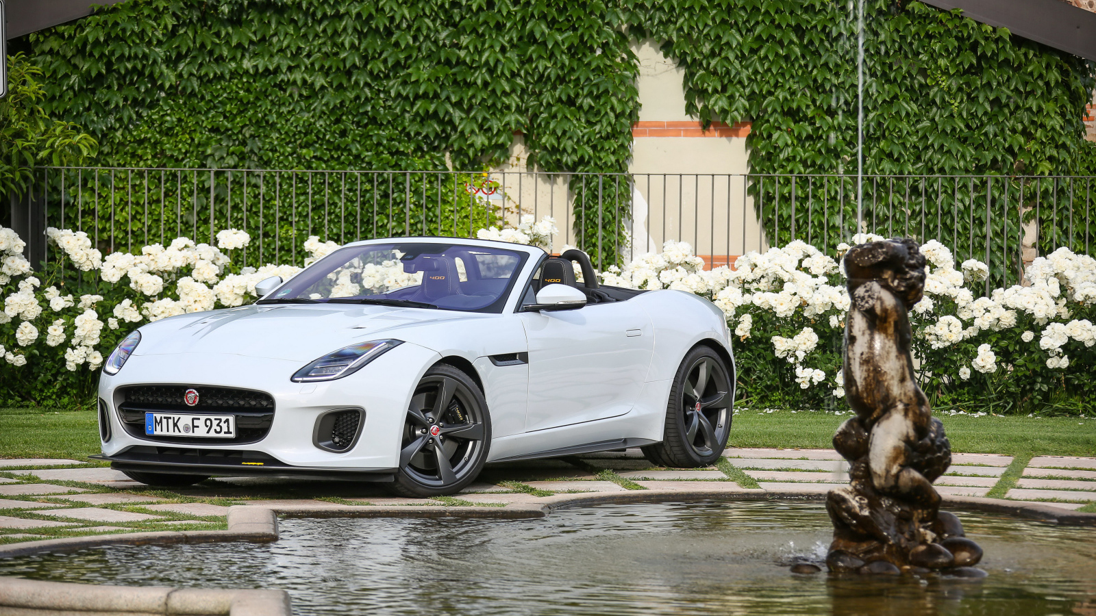 Белый автомобиль кабриолет Jaguar F-Type у фонтана