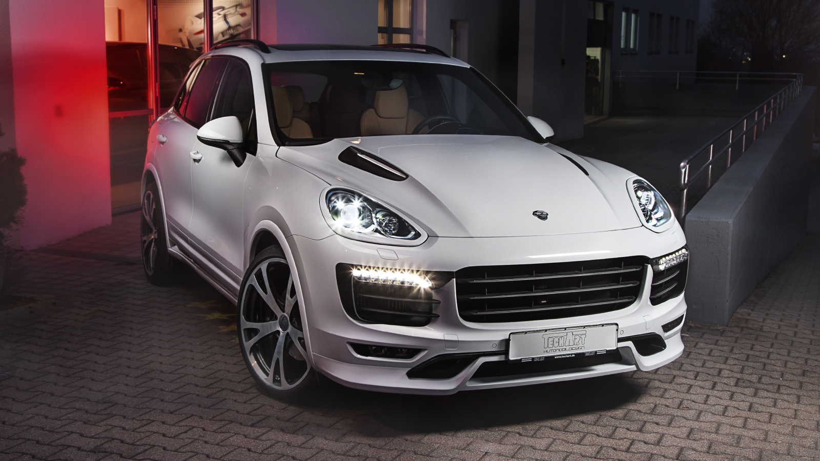 Белый внедорожник Porsche Cayenne с включенными фарами