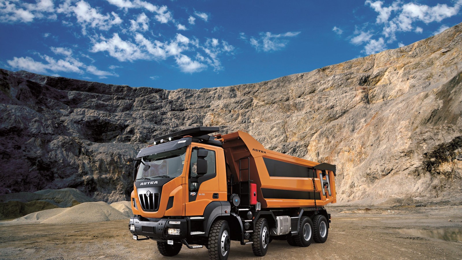Оранжевый грузовик Astra HD9 84.50 8×4 в карьере под голубым небом