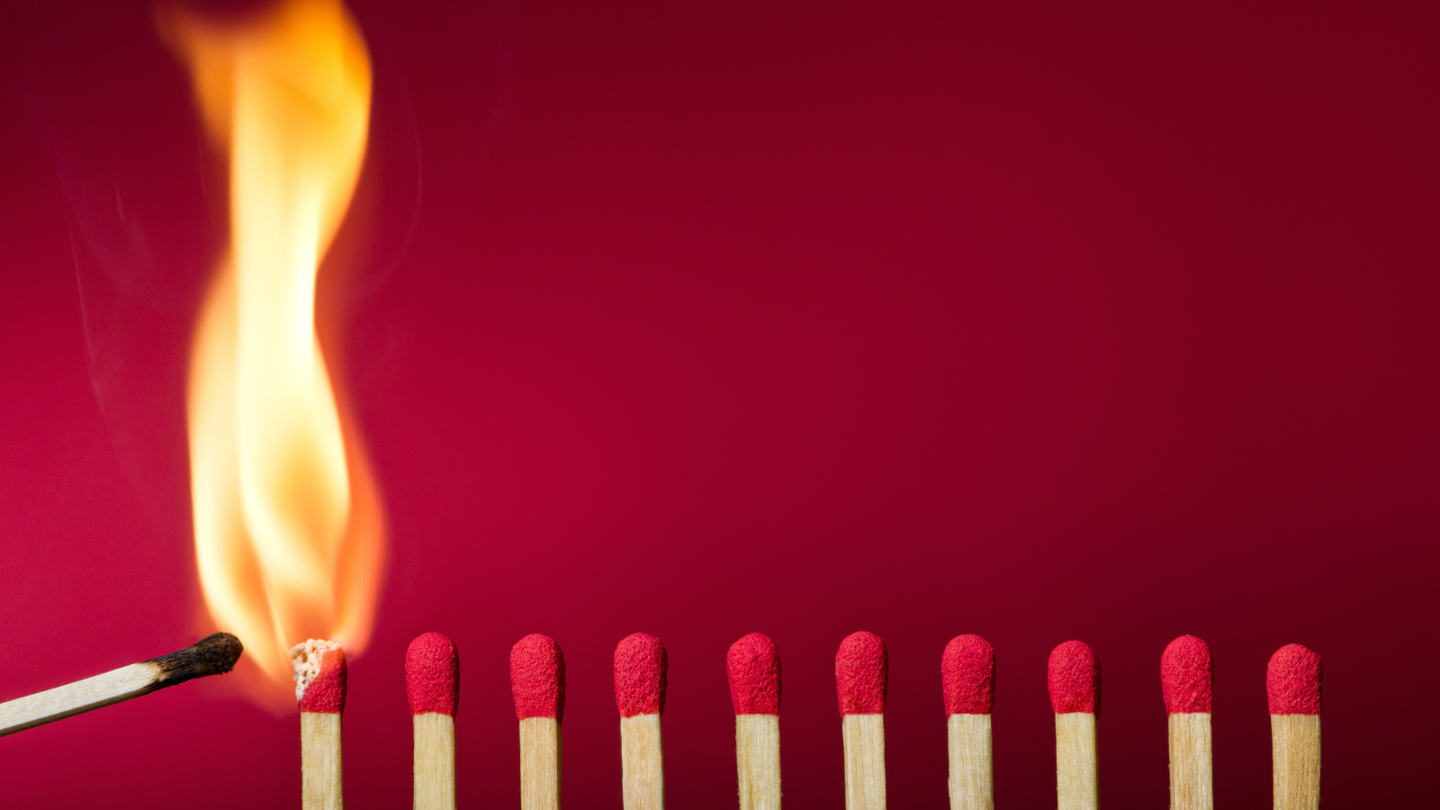 Зажженная спичка и спички на красном фоне
