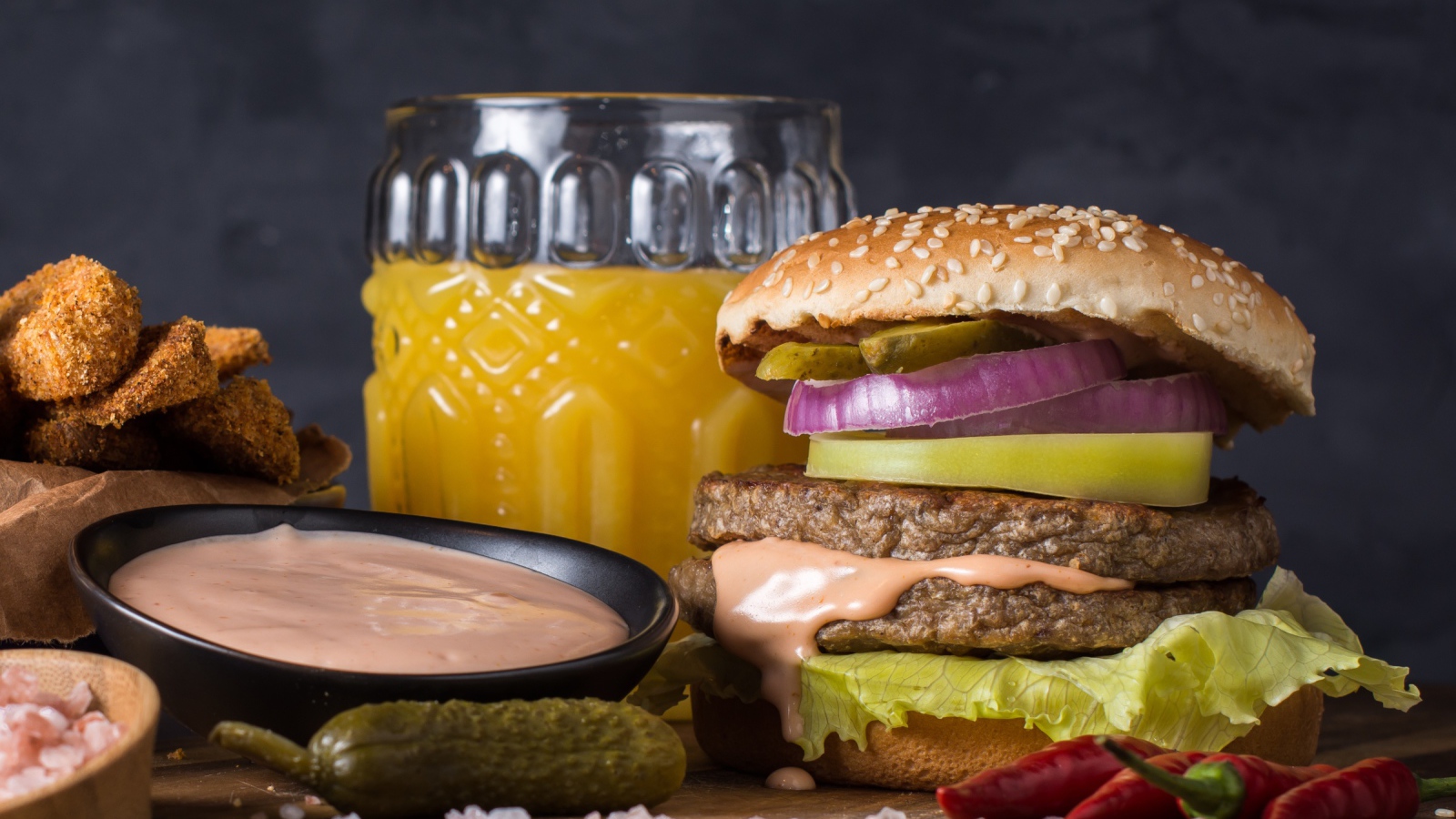 Аппетитный гамбургер на столе с соусом, овощами и соком