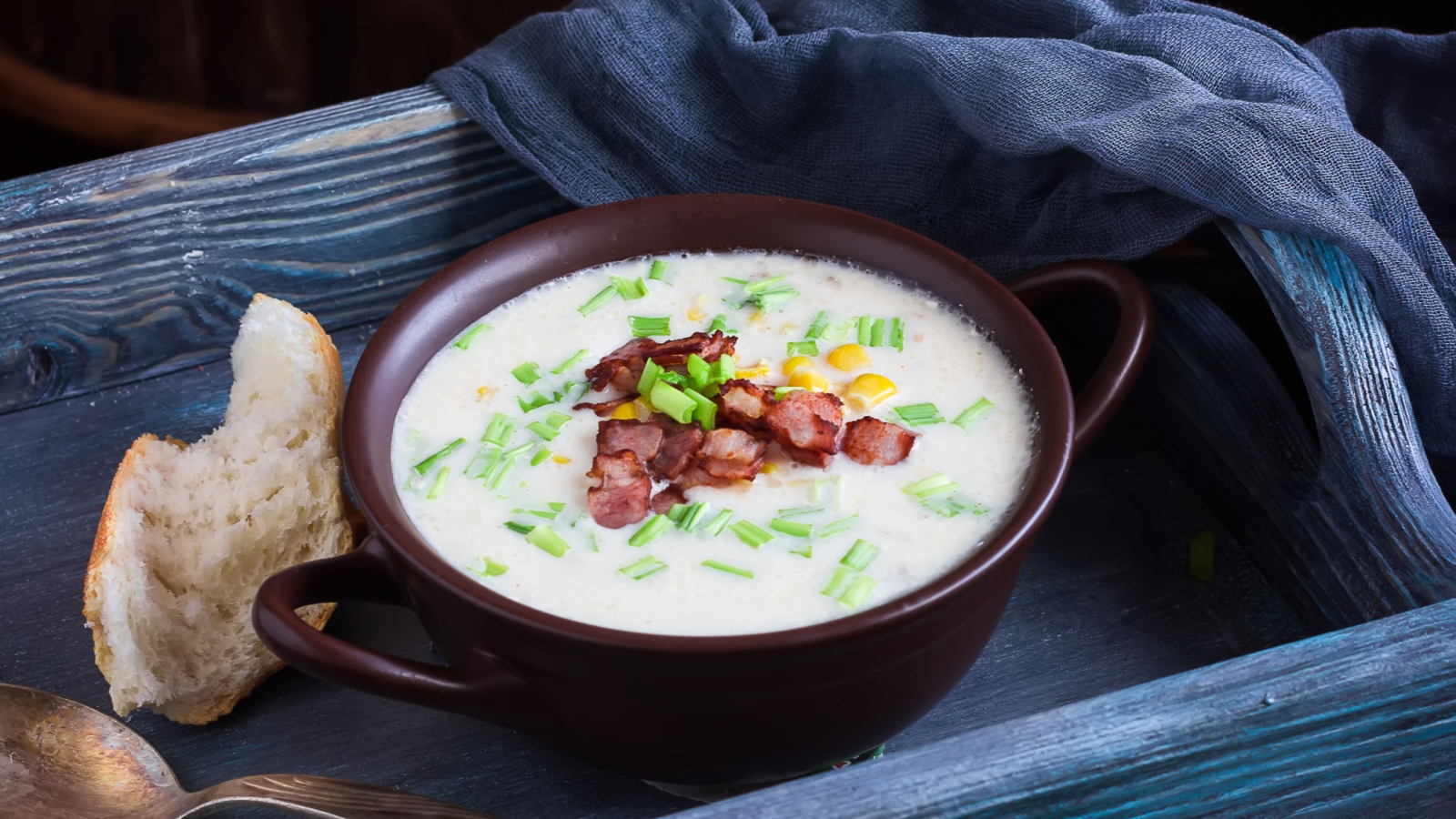 Сырный суп с зеленью и беконом на столе с куском хлеба