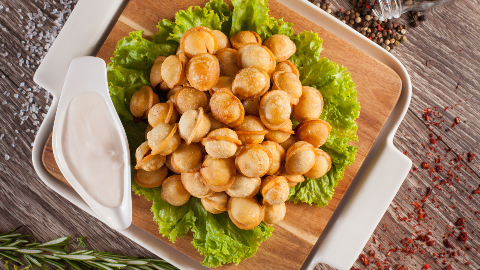 Пельмени с соусом и листьями салата лежат на разделочной доске