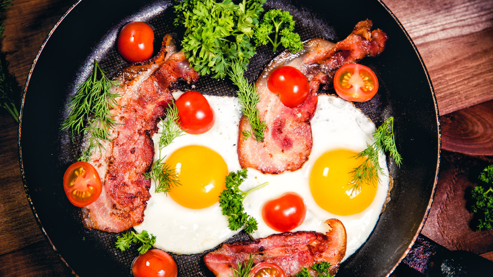 Яичница с беконом, помидорами и зеленью в сковороде на завтрак