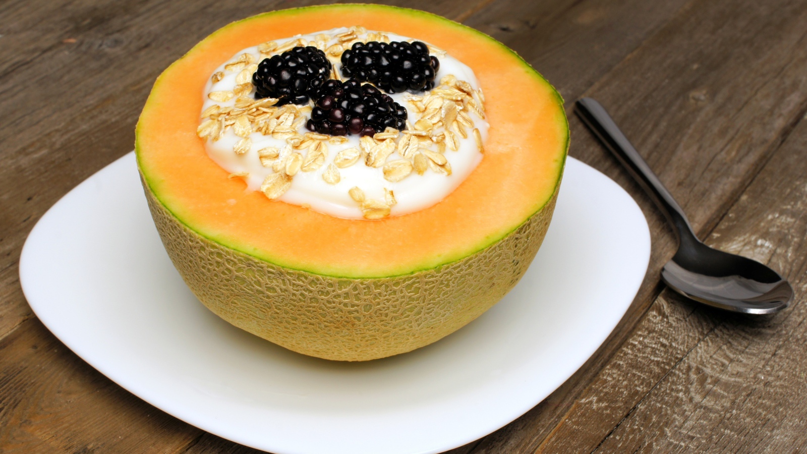 Йогурт с ежевикой и овсянкой в тарелке из свежей дыни на завтрак