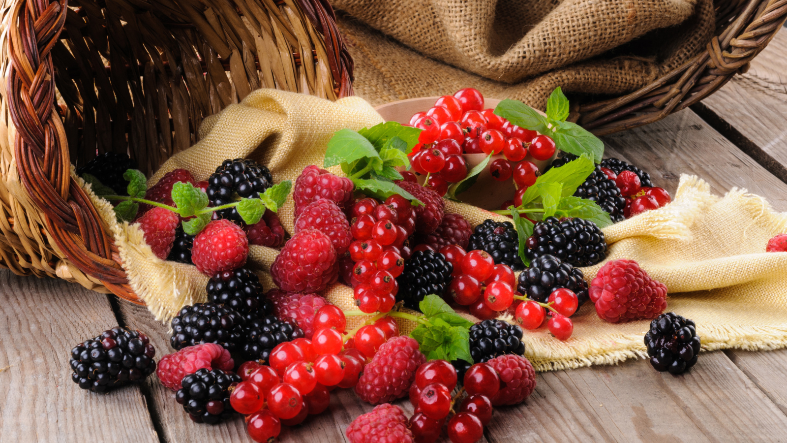 Свежие ягоды ежевики, малины и красной смородины с корзиной на столе