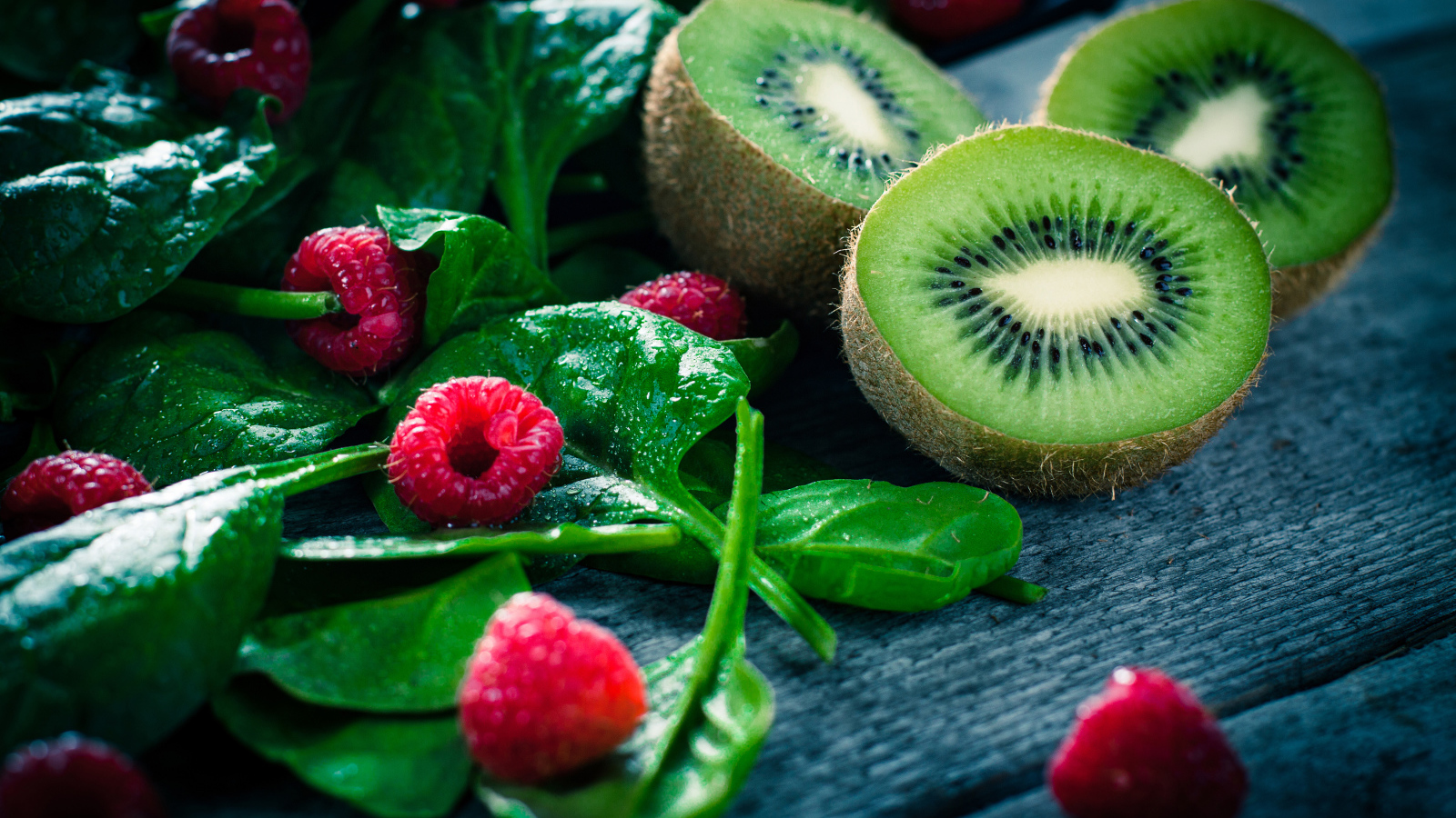 Половинки киви на столе с зелеными листьями и свежей малиной