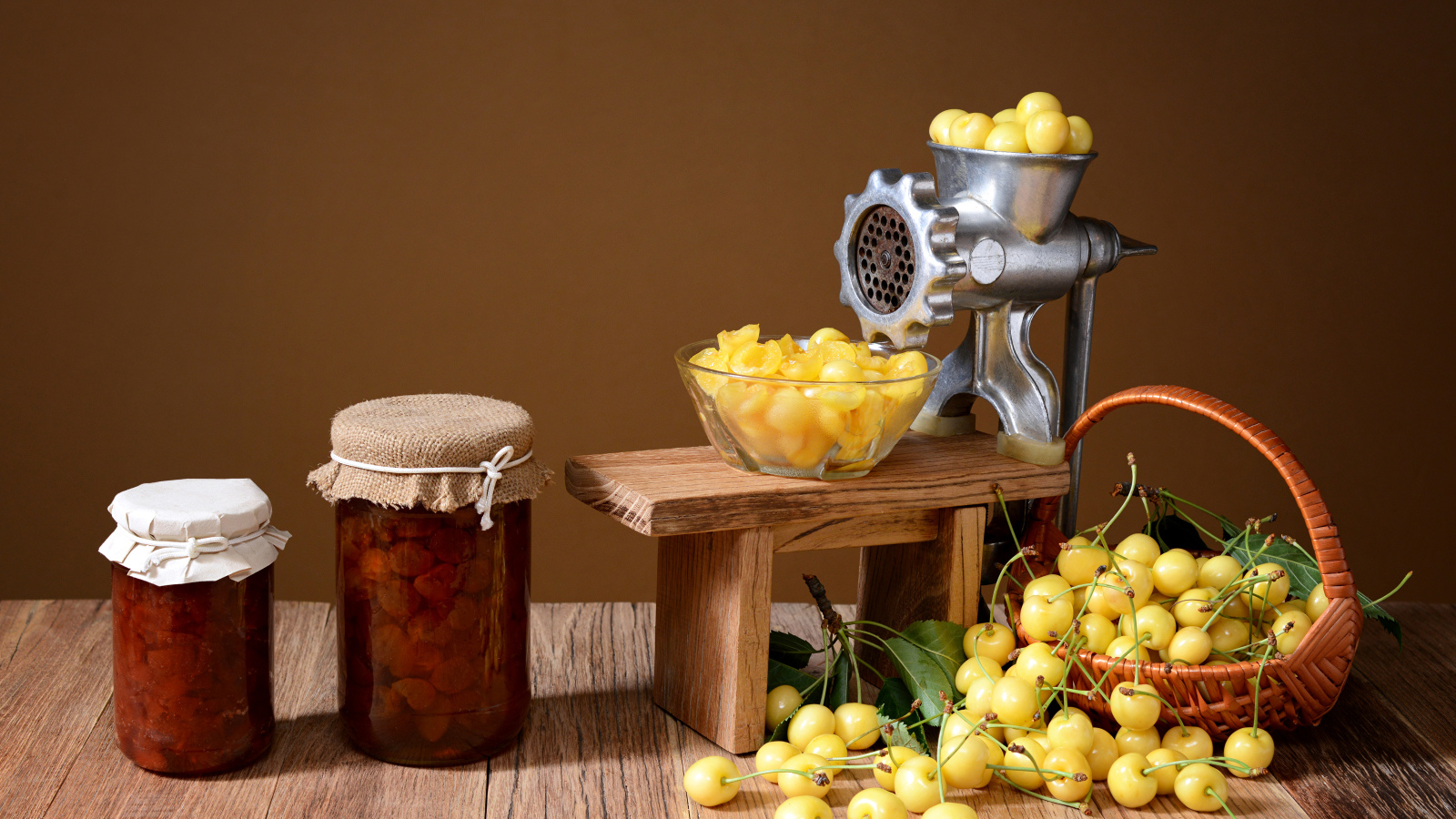 Две баночки варенья и желтые черешни на столе с мясорубкой
