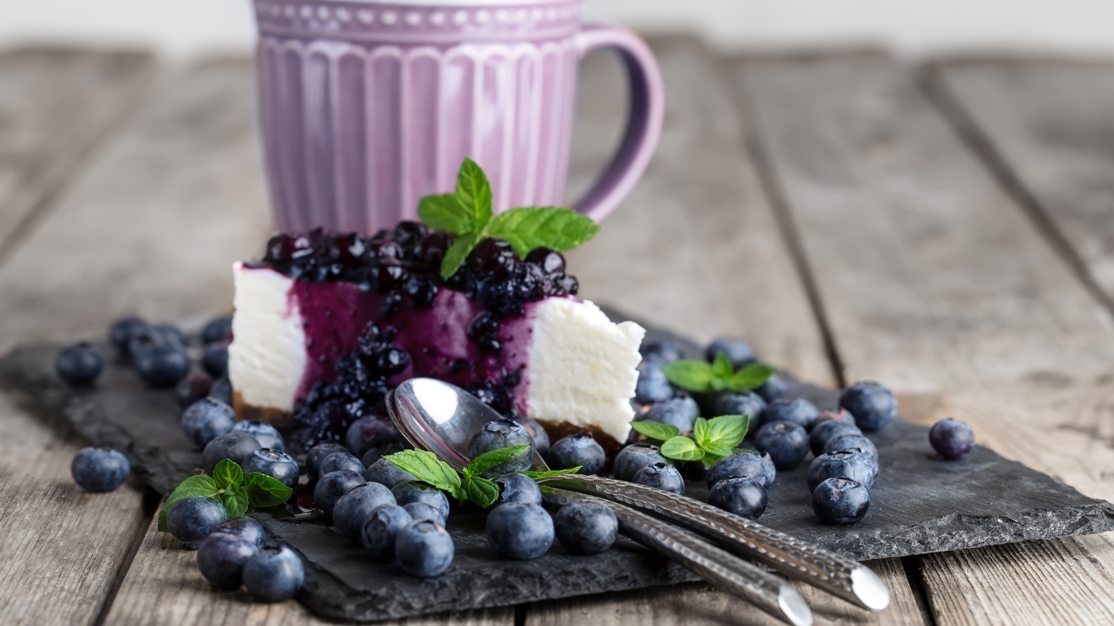 Черничный чизкейк со свежими ягодами лежит на столе с чашкой