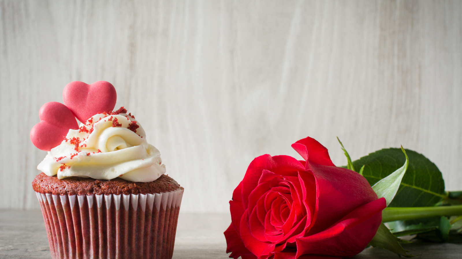 Капкейк с кремом и красной розой на столе