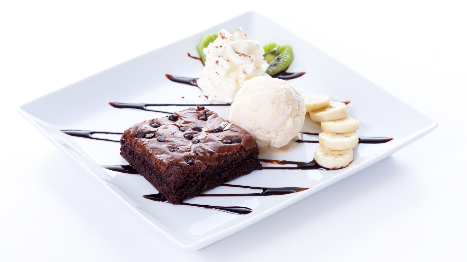 Шоколадное пирожное с мороженым, сливками и кусочками банана на белой тарелке