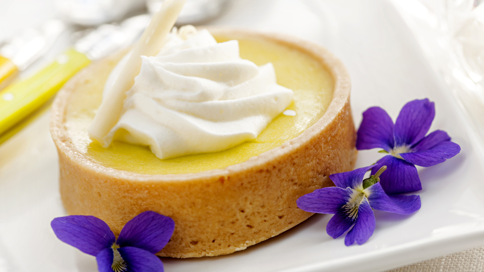 Десерт с кремом и фиолетовыми цветами на белой тарелке
