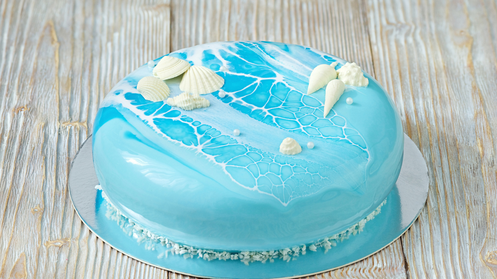 Глянцевый торт голубого цвета украшен сахарными ракушками