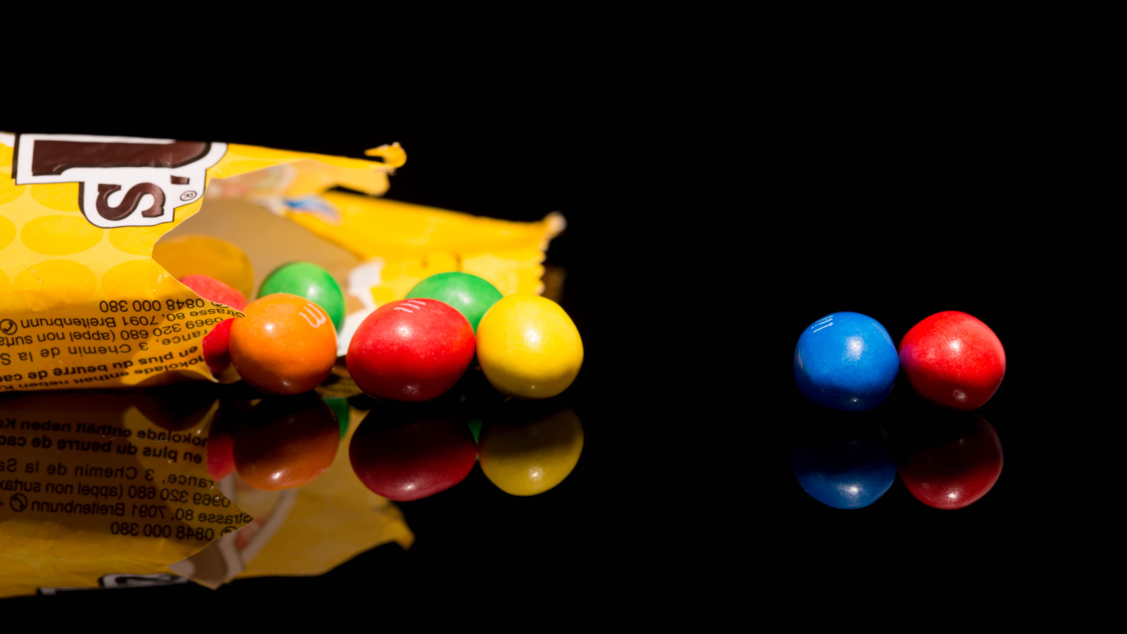 Разноцветные конфеты  M&m's отражаются в черной поверхности стола 