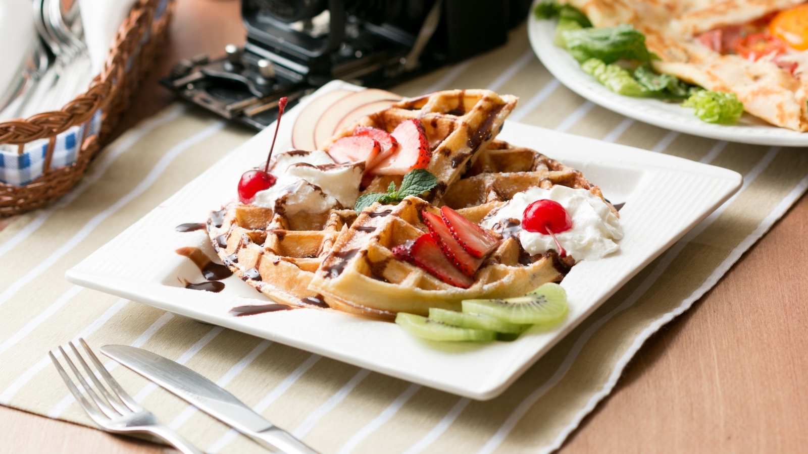 Сладкие вафли с ягодами клубники, вишни и кусочками киви на тарелке