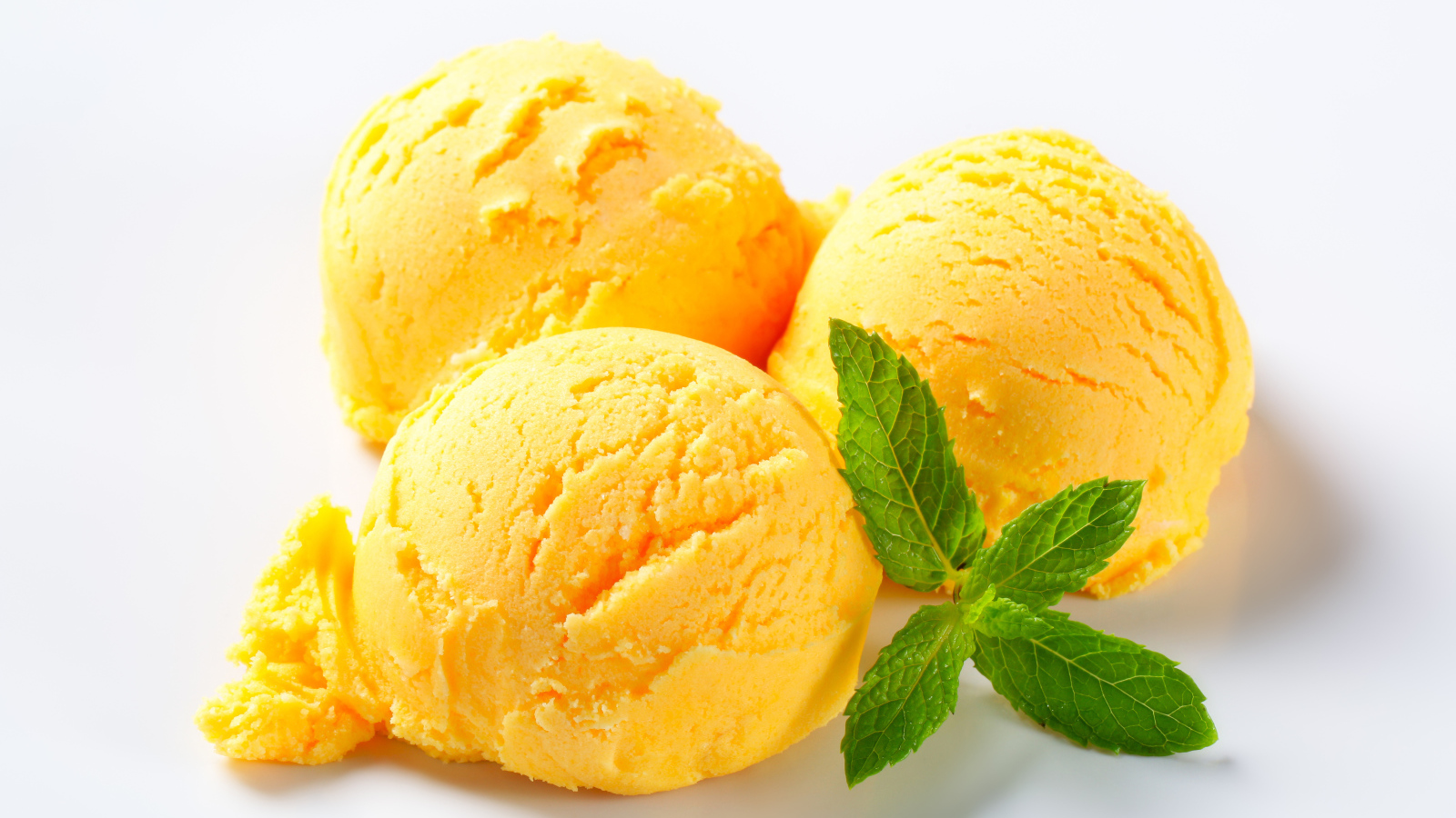 Три шарика фруктового мороженого с листиком мяты на белом фоне